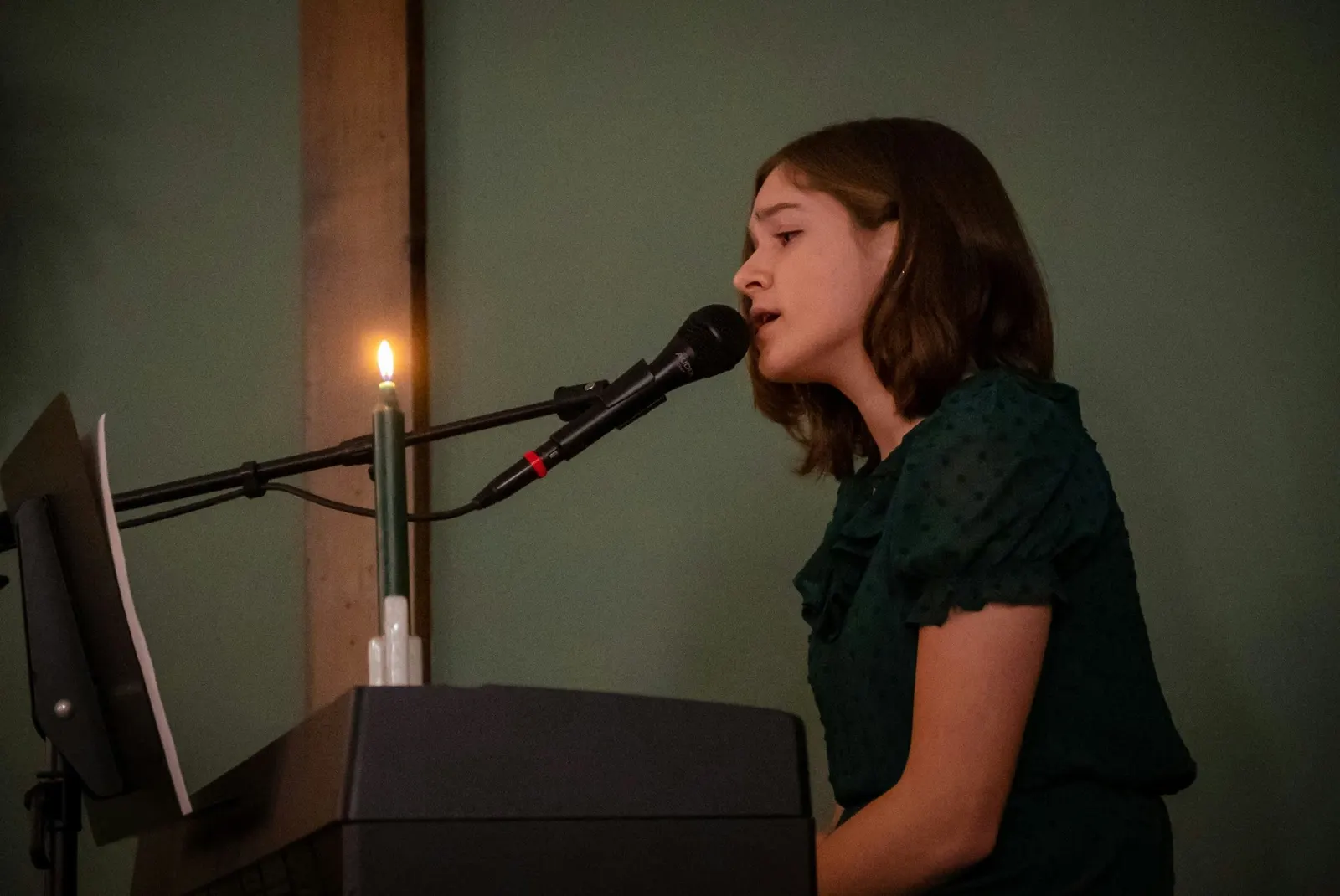 A young singer performing at a keyboard with a microphone and a lit candle